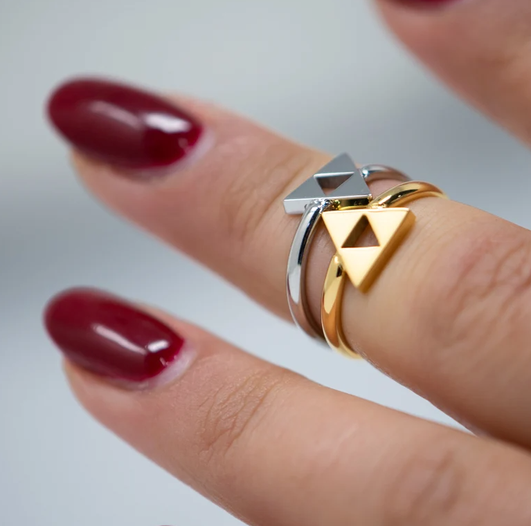 a silver and a gold triforce ring on a finger