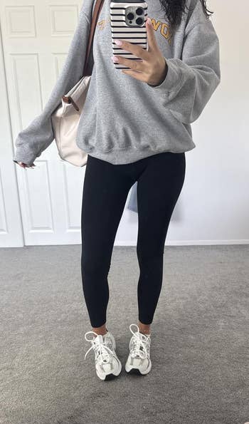 Person successful a casual outfit with a sweatshirt, leggings, and sneakers takes a reflector selfie, showcasing a casual athleisure look