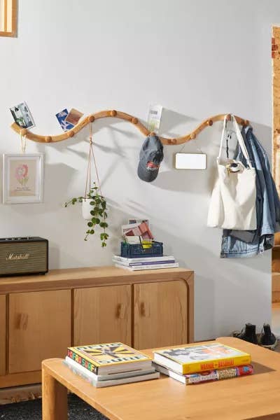 Wall-mounted branch serving as a unique clothing rack with various items hung on it and a wooden cabinet below. Great for organizing small spaces