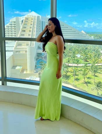 Woman in elegant strapless yellow gown posing by a window overlooking a sunny resort view