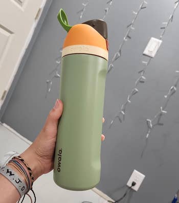 reviewer holding the water bottle in the green/orange color