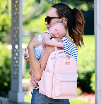 mother wearing pink diaper bag mini backpack, carrying baby
