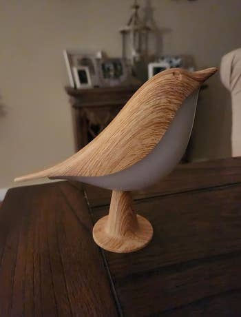 Small light wood bird shaped light propped on a table 