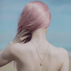 Model wearing pink gemstone necklace with gold taurus tattoo on neck