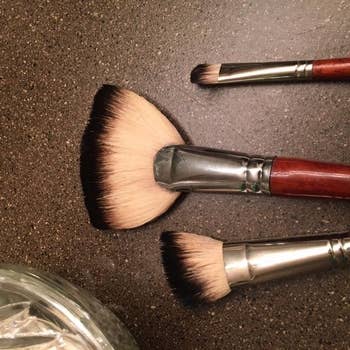 Three constitution  brushes of antithetic  shapes connected  a countertop adjacent  to a solid  jar