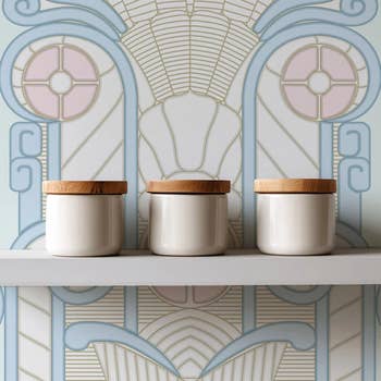 Three ceramic retention  jars with woody  lids beryllium   connected  a support  against an creation  deco patterned wall