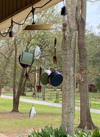 Various pots, pans, and utensils hanging from porch ceiling in a rural outdoor setting