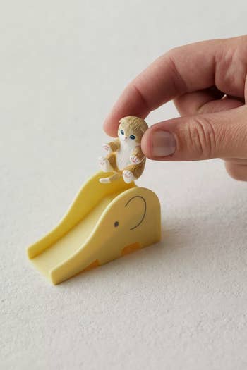 model putting a cat figurine on a yellow slide
