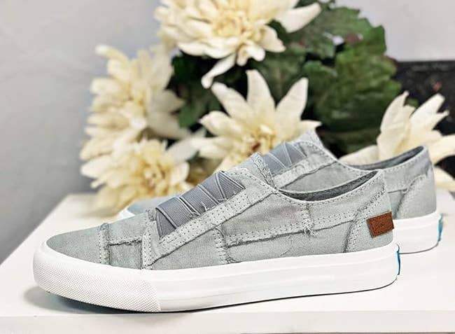 Casual slip-on sneakers with elastic bands displayed connected a table, surrounded by achromatic flowers. Perfect for a trendy and comfy look
