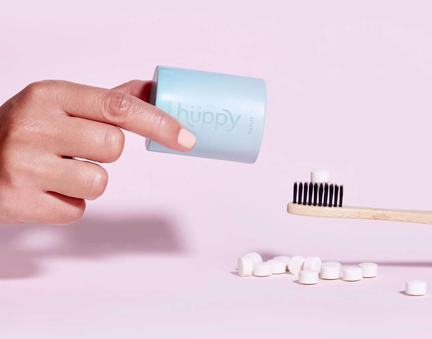 a model's hand holding a case of huppy next to a toothbrush with a toothbrush tablet on top of it