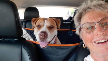 reviewer smiling with a dog in a car. Dog is seated with tongue out, behind a seat protector.
