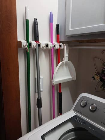 reviewer image of brooms hanging from the organizer mounted to a wall in a laundry room