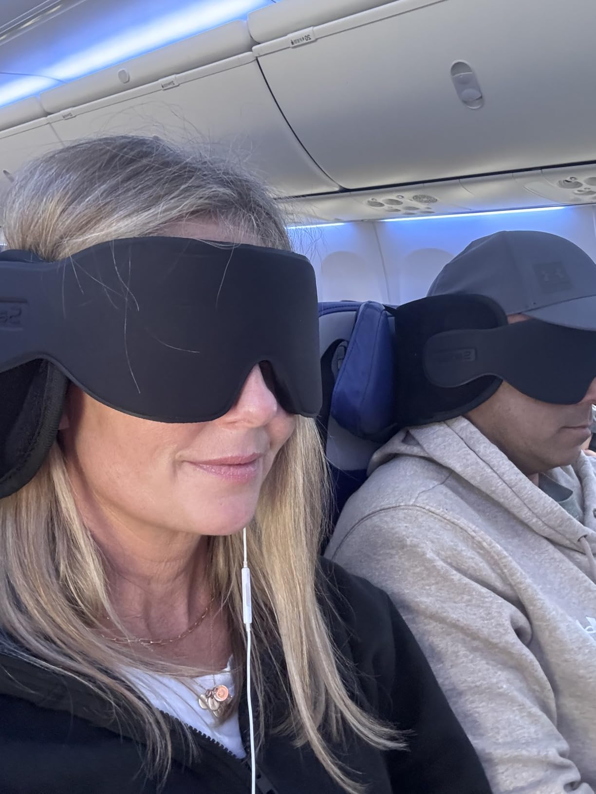 reviewers sitting in a plane using the neck pillow-eye mask