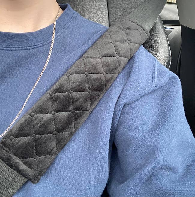 Close-up of a person wearing a blue sweatshirt and a seatbelt with a black quilted shoulder pad