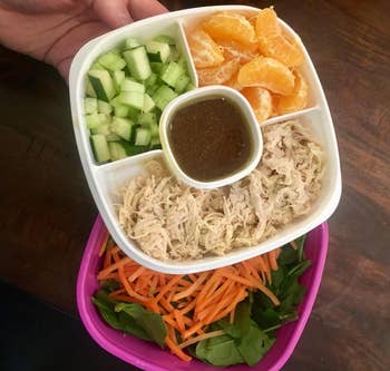 A purple container with a bottom full of salad and a top with four sections dividing ingredients 