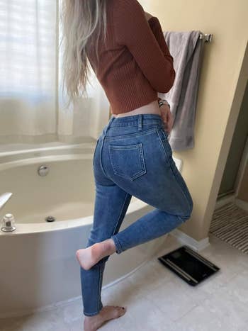 Person successful ribbed sweater and jeans stands connected 1 ft successful a bath adjacent a tub, showcasing casual benignant for a manner article