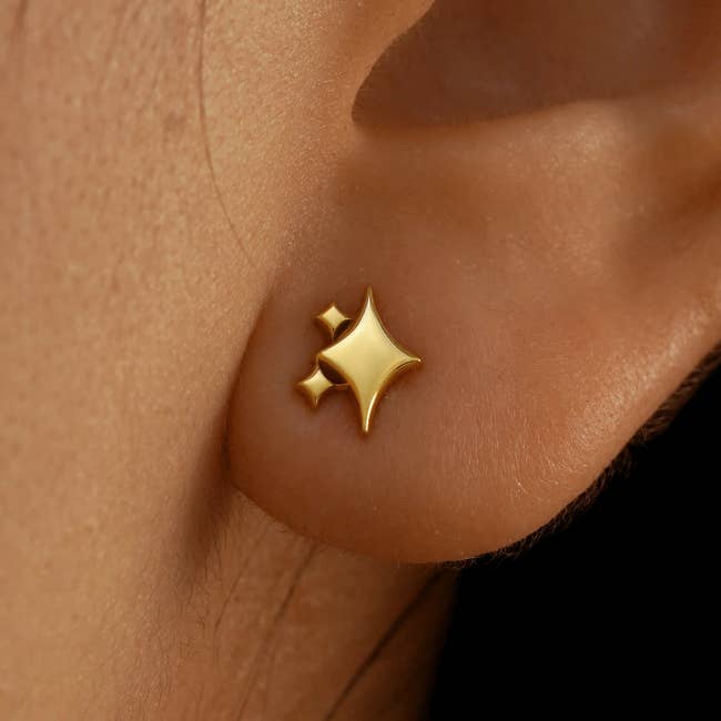 Close-up of a golden star-shaped earring worn connected an ear, highlighting its sleek design