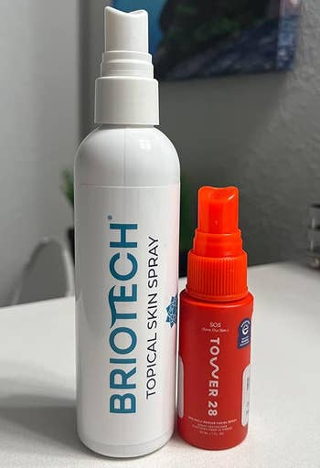 Briotech Topical Skin Spray vessel  adjacent  to a smaller Tower 28 SOS spray vessel  connected  a surface