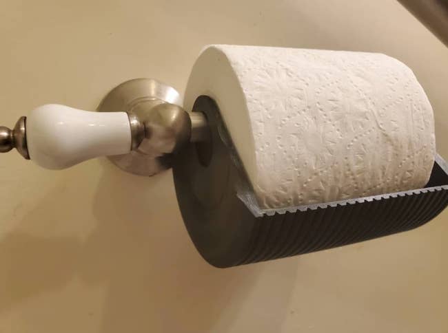 a black plastic cover around the bottom of a roll of toilet paper 