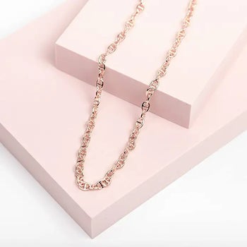 a rose gold chain necklace laying on two pink boxes