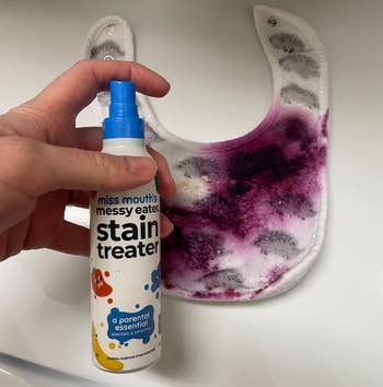 reviewer holding a bottle of stain remover spray beside a bib with a purple stain