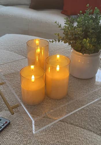 Three lit candles and a tiny  works  connected  a wide   tray placed connected  a cushioned surface. Remote power  disposable   connected  the near  side