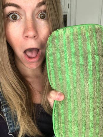 a reviewer with a shocked face showing the dirty reusable mop pad after using it