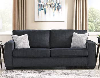 a black two-seater sofa with two throw pillows on it