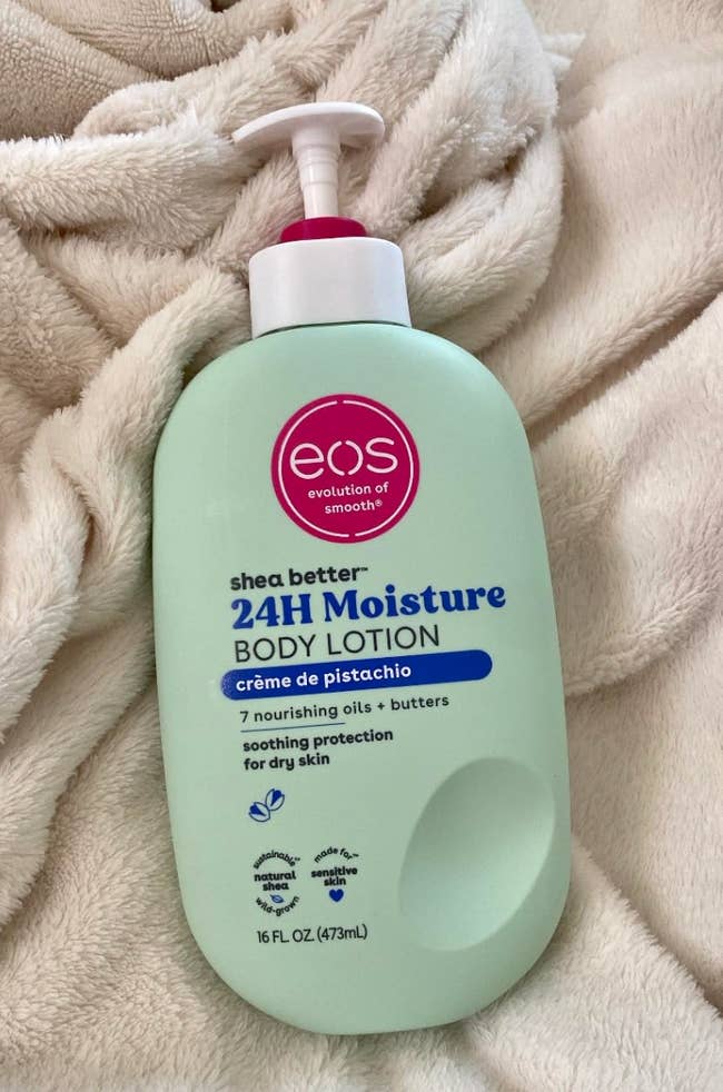 Bottle of EOS Shea Better 24H Moisture Body Lotion, Crème de Pistachio, connected a fuzzy blanket. Suitable for adust skin