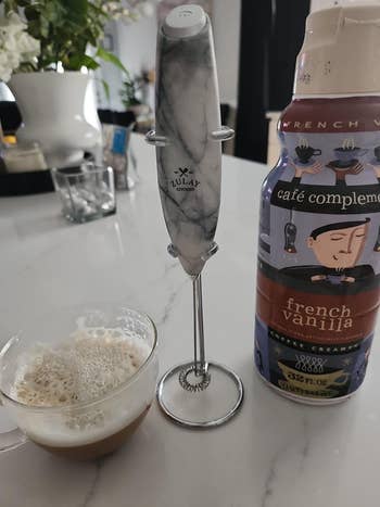 Marble-patterned milk frother with stand, alongside a cup of frothed milk and a French vanilla creamer bottle on a kitchen counter