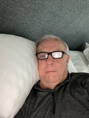 Man lying connected pillow, wearing glasses and a zippered sweater
