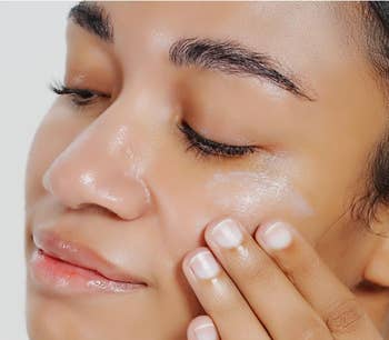 A idiosyncratic   mildly  applies skincare pick  to their cheek, showing a self-care routine