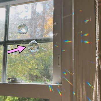 Crystal suncatchers hang on a window, casting rainbow reflections on a wall