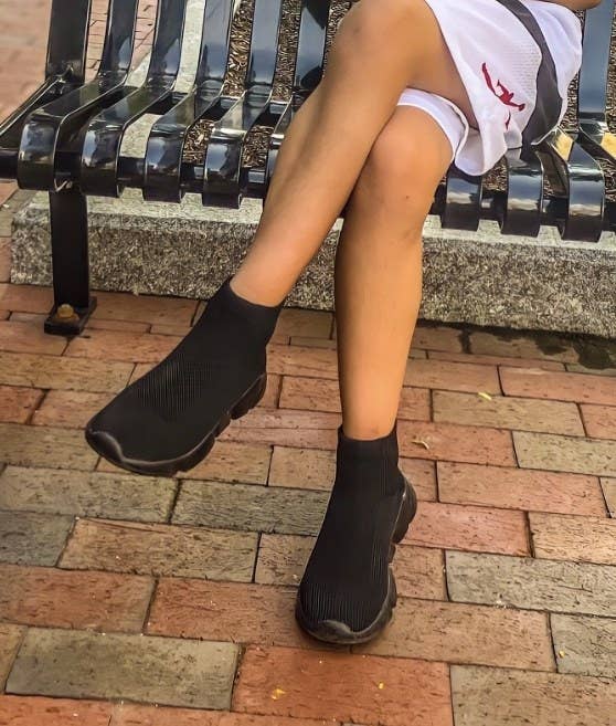 Person sitting on a bench wearing sleek, slip-on black sneakers with shorts, featured in a shopping article