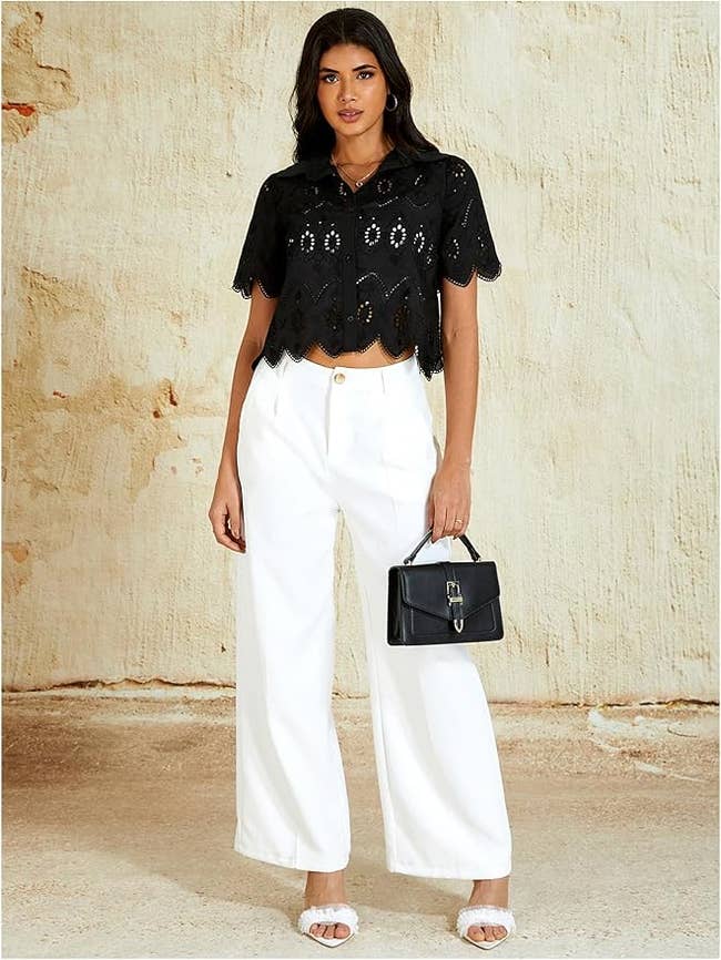 Model wearing a lace harvest top, wide-leg pants, and holding a tiny handbag, posing for a manner shoot