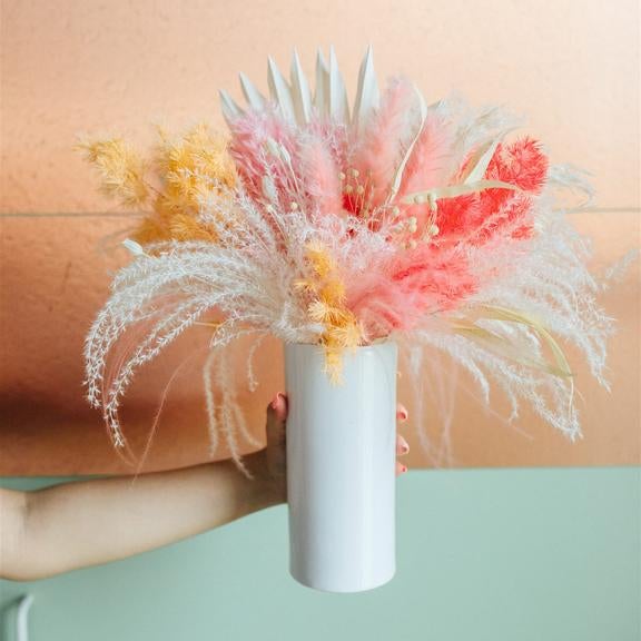 person holding vase filled with dried flowers