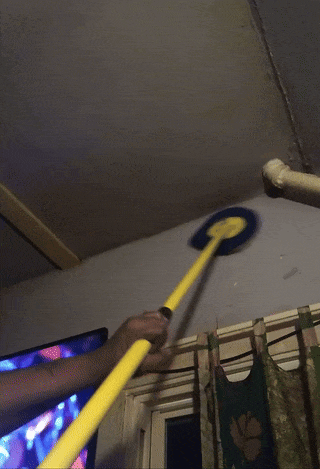 Someone is utilizing a yellowish  mop to cleanable  a ceiling adjacent   pipes successful  a room