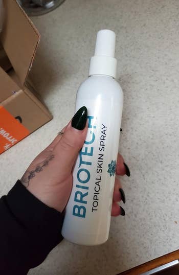 Hand holding bottle of Briotech Topical Skin Spray on a counter