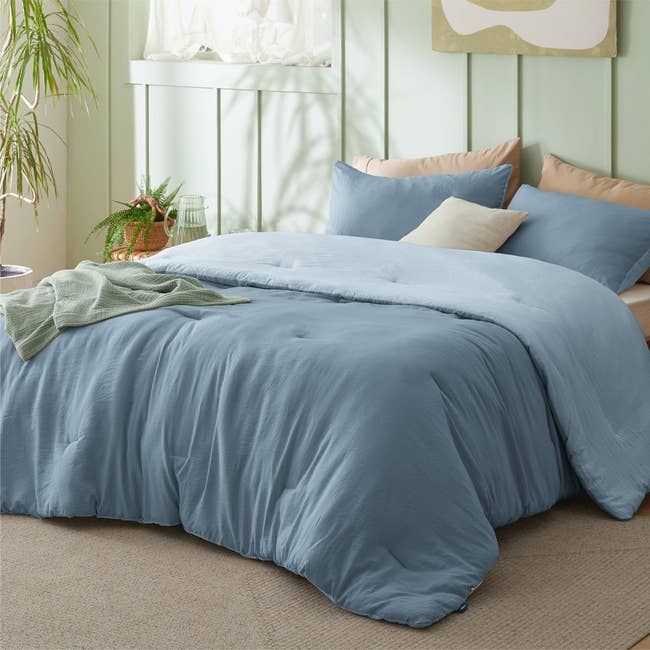 Cozy bedroom setup featuring a neatly made bed with a plush comforter and soft pillows, accented by a plant and natural light from a nearby window