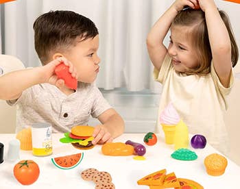 Two children playing with pretend food while sitting at a table