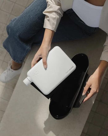 Model holding a square shaped flat white matte flask-style water bottle over their laptop bag 