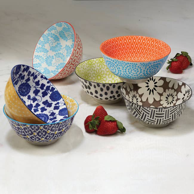A radical  of decorative bowls with assorted  intricate patterns displayed adjacent  to caller  strawberries connected  a marble surface