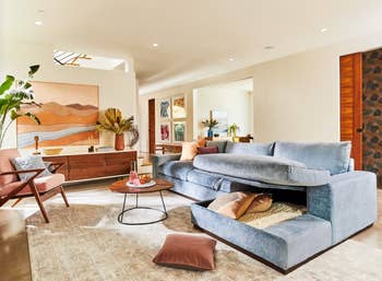 Modern living room with a plush sectional sofa, decorative pillows, wooden furniture, and abstract art. Room is styled for a cozy, inviting atmosphere