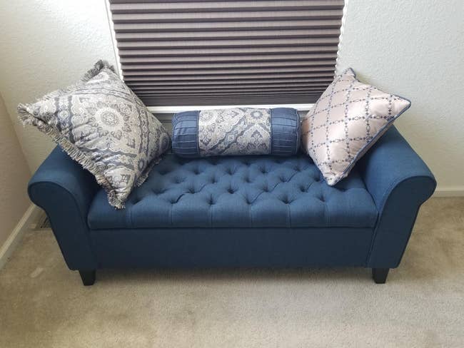 reviewer image of the ottoman with a few throw pillows on top of it