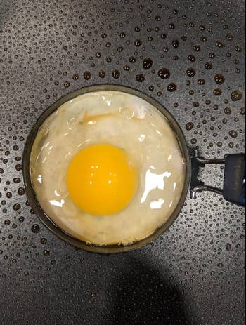 An egg cooking in a ring shaped mold 