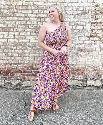 a reviewer wearing a one-shoulder dress in a multicolor floral print 
