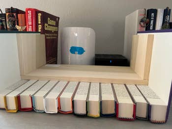 Books arranged on a shelf with a wooden bookend holder. Titles are visible and include various genres, such as strategy and personal development