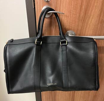 reviewer's black garment duffle bag hanging on a door handle
