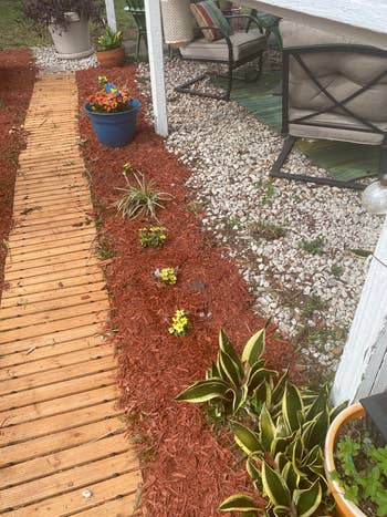 Outdoor patio with a wooden path, potted plants, and a seating area featuring cushioned chairs