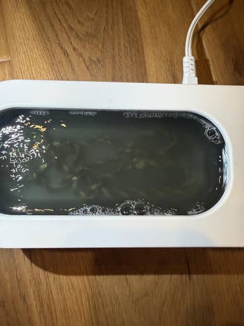 Device cleaning jewelry successful soapy water, situated connected a woody surface, plugged successful and operating